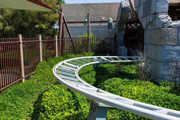 Curved Rollercoaster at a theme or amusement park empty white tracks and grass and blue sky background.