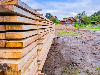 Lumber. Wooden beams are stored outside. Concept - preparation of materials for building a house. Construction of a house in a cottage village. Lumber warehouse in a cottage village. Lumber on ground