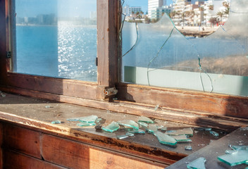 Vandalism broken window glass with pieces of glass in the foreground. In the background, the Mediterranean Sea is out of focus