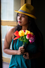 Portrait of an Asian/Japanese/Korean brunette young girl in greenish blue  western dress with yellow hat front of a window inside of a room. Fashion and cosplay photography.