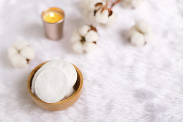 Obraz na płótnie Canvas Cotton facial pads for removal makeup with natural cotton flowers and candle on white fur background, hygiene and healthy care lifestyle