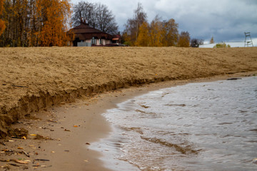 Waves wash away the sand on the beach near the river Bank. Surf. Autumn. Leaves of trees turn yellow.