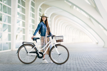 Teen girl with patterned dress and hat waits for a friend to go for a ride with her urban bicycle. Outdoor and fun concept in spring and summer