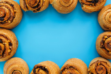 Cinnamon rolls, nuts, raisins and lemon slices on a blue background with a copy of the space. Modern concept of nutrition. Frame of sweets for decoration, layout for the designer
