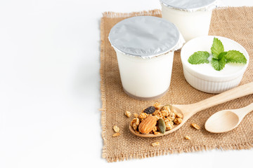 Healthy flavored yogurt in plastic cup and ceramic bowl with granola in wooden spoon on the sackcloth on white background for organic food healthy with copy space for text.