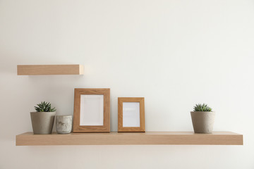 Wooden shelves with plants and photo frames  on light wall