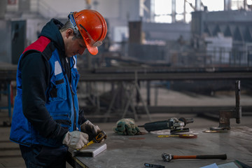The builder measures the stainless steel profile at the workplace in the production shop, measuring...