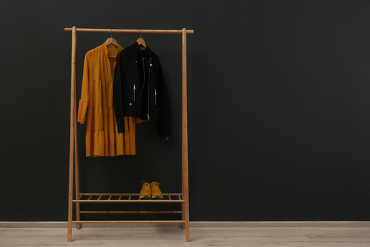 Rack with stylish clothes near black wall. Space for text
