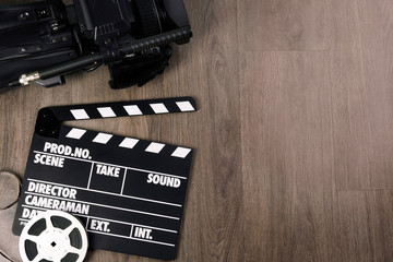 Modern video camera, movie clapper and reel on wooden table, flat lay. Space for text