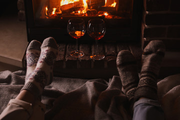 Couple and glasses of red wine near burning fireplace, closeup