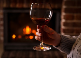 Man with glass of wine near fireplace at home, closeup