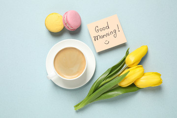 Delicious coffee, macarons, flowers and card with GOOD MORNING wish on light background, flat lay