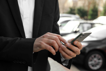 Businessman ordering taxi with smartphone on city street, closeup