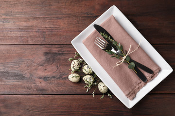 Festive Easter table setting with quail eggs and floral decor on wooden background, flat lay. Space for text