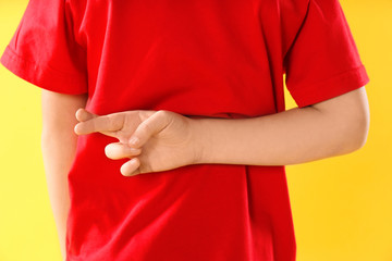 Little boy with crossed fingers on yellow background, closeup. April fool's day