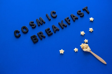 top view flat lay wooden spoon with crunchy corn stars and inscription cosmic breakfast on a blue background , space day card
