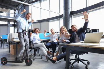 Five happy modern business people are keeping arms raised and expressing joyful while sitting in large office.
