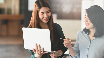 Young graphic designer holding and showing a computer laptop to her manager while standing at the modern meeting table with comfortable office as background.