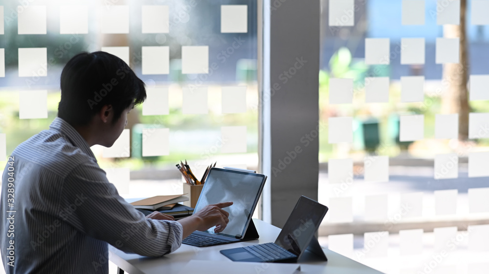 Poster photo of businessman using/typing on computer tablet with keyboard case while sitting at the modern 