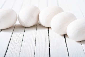 white painted wooden eggs on bright wood table background