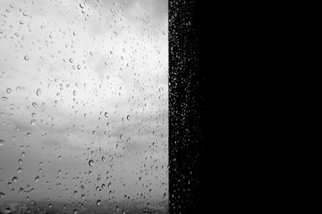 Raindrops on the dark window. Half a wet window. Black and white photo of rain. Dark background.
