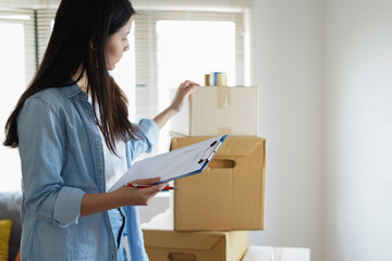 Asian woman checking and packing the carton box prepare to move to new house relocation shipping or...