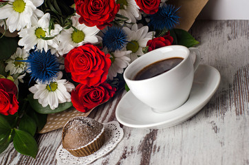 Cup of coffee with fresh cupcake and bouquet of flowers