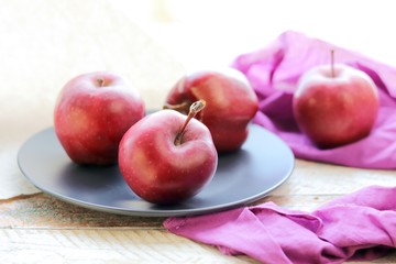 Red fresh apples on a plate, bright cloth on a wooden windowsill, healthy food
