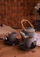 wooden table prepared for tea time. teapot, glasses of hot tea, book and flowers. in the light of the romantic candle giving a warm and welcoming tone to the scene. Chocolate cookies, and tea filter.