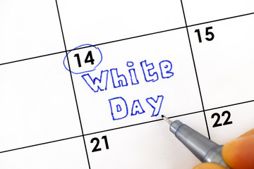 Woman fingers with pen writing reminder White Day in calendar.