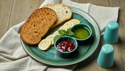 Toasted slices of bread with spiced butter, jam and honey on a turquoise plate on a wooden background. Continental breakfast. Close up view