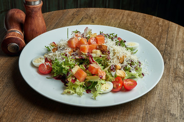 Close up view on served Caesar salad with smoked Salmon in white plate on wooden background. Tasty seafood salad.