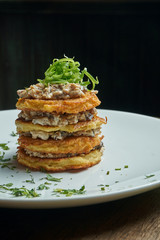 Close up view on Traditional dish of Ukrainian cuisine - potato pancakes with sour cream and mushroom on a white ceramic plate on rustic background