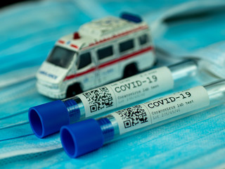 Test tube sample coronavirus test on background from face masks with ambulance car in the background