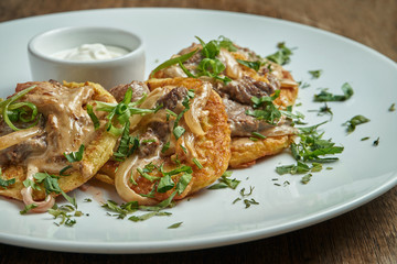 Close up view on Traditional dish of Ukrainian cuisine - potato pancakes with sour cream and beef on a white ceramic plate on rustic background