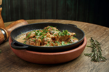 Baked potatoes with chicken in a creamy sauce in a pan on a wooden background. Close up, selective focus