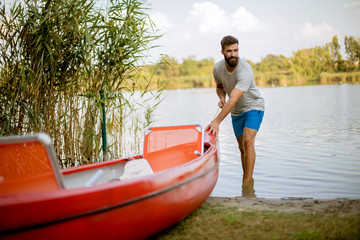 Young man pulling canoe into calm lake