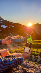 A man holding a plate filled with pasta and in the other hand a bottle of wine with the sun setting...