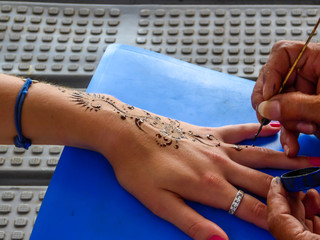 07282018/Lombok/Indonesia: A girl having a henna tattoo done on her hand. The pattern goes through her hand and fingers. She has a blue bracelet and a silver ring. Nails are polished pink.