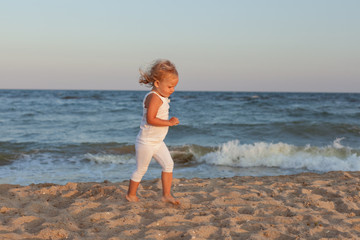 Little beautiful girl runs on the sandy seashore.