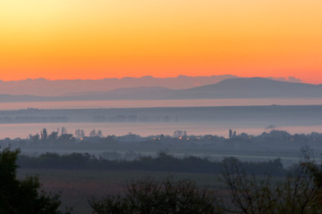 layered rural landscape with sunset colours and mist, giving a feeling of heat and the peak of summer.