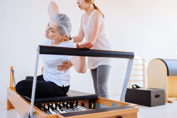 Personal trainer assist senior woman exercising on machine at gym