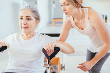Fototapeta premium Personal trainer assist senior woman exercising on machine at gym