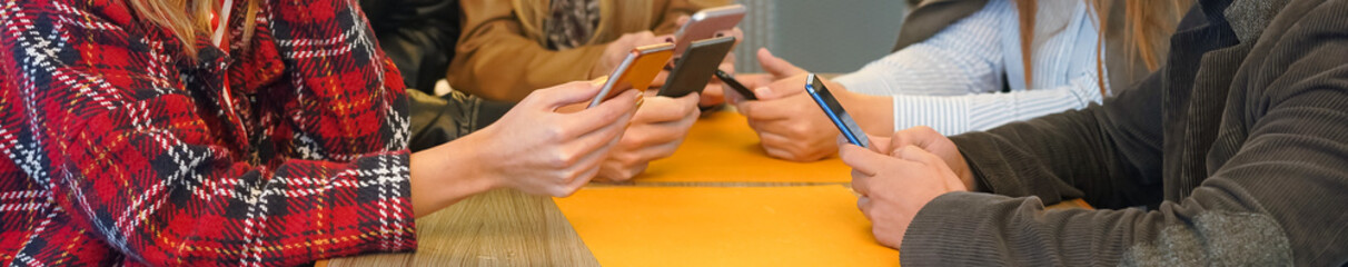 Group of people sitting around the table while holding smartphones - Teenagers obsessed with...