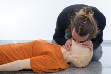 Man teaching cardiopulmonary resuscitation with a dummy on a white background. Doing Mouth-to-mouth...