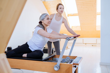 Active senior woman working exercise in the gym. Personal trainer helping senior woman. Workout in gym.