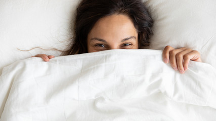 Close up top view portrait of smiling Caucasian young woman lying in white comfortable bed look at...