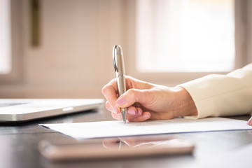 Businesswoman's hand while writing something with pen
