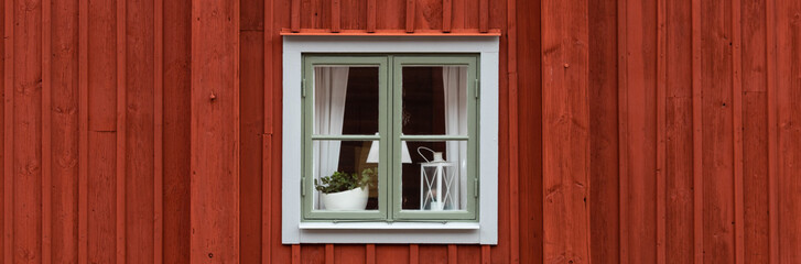 White framed window on an old red plank wooden cottage. Lamp, candleholder and plant in the window