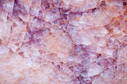 Full frame close-up background of the textured fissures in a slab of pink and purple rock crystal